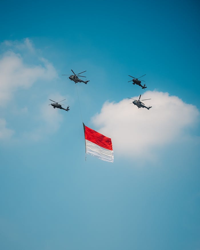 Four helicopters fly with the Indonesian flag against a blue sky during Independence Day celebrations in Jakarta.